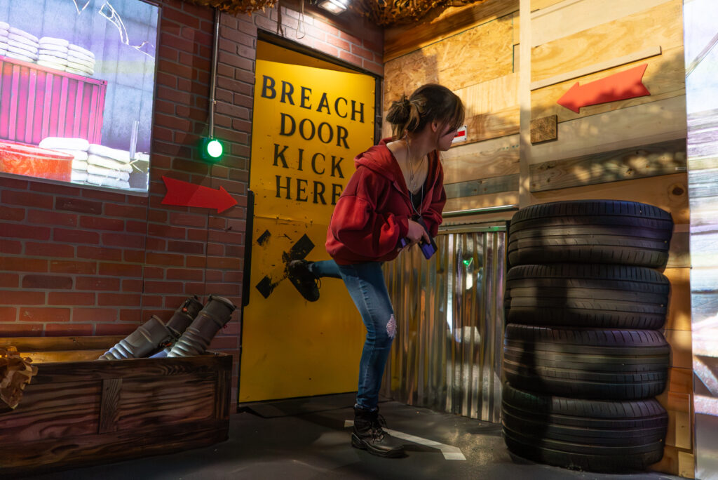 Participant kicking breach door during tactical training at Decision Tactical indoor theme park in Sanford, North Orlando