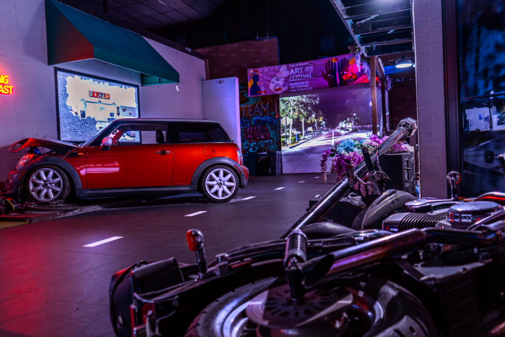 Purpose-built indoor street scenario at Decision Tactical in North Orlando, featuring a red car with its hood open, a toppled motorcycle, storefronts, graffiti, and a festival banner set up for law enforcement scenario training.