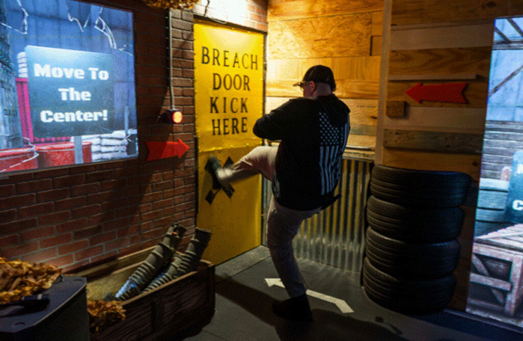 Participant kicking a yellow breach door during a tactical challenge course at Decision Tactical, an indoor tactical theme park in North Orlando