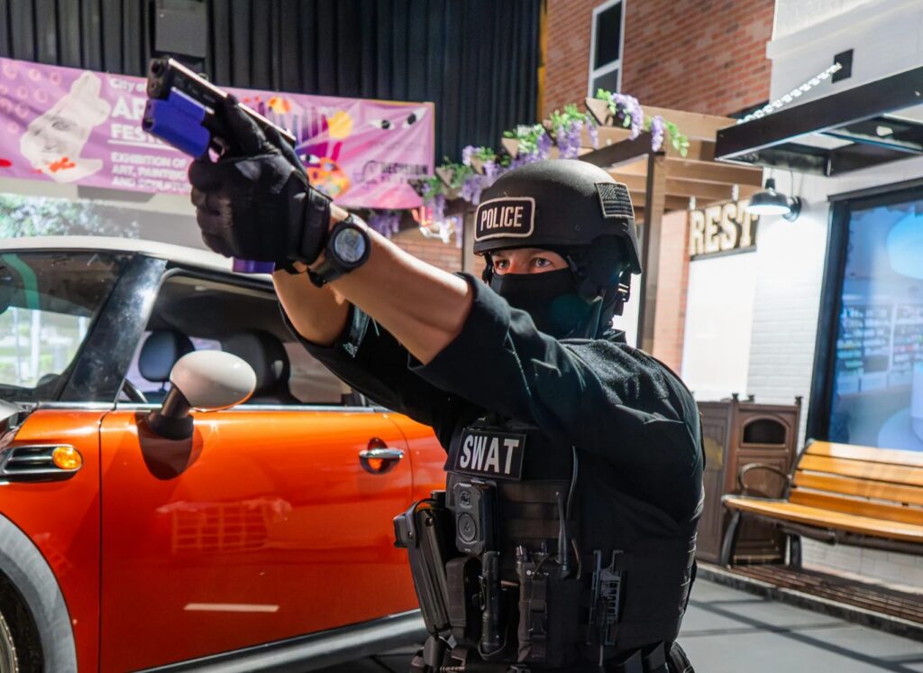 SWAT Officer Training in the Street Scenario at Decision Tactical in North Orlando - Decision Tactical | Indoor Theme Park SWAT officer kneeling behind a car and aiming a training pistol during the street scenario at Decision Tactical in North Orlando